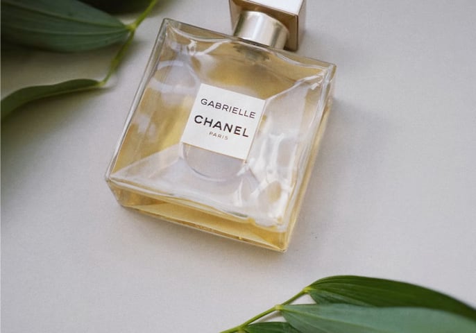 A bottle of Chanel Gabrielle perfume in between two palm leaves